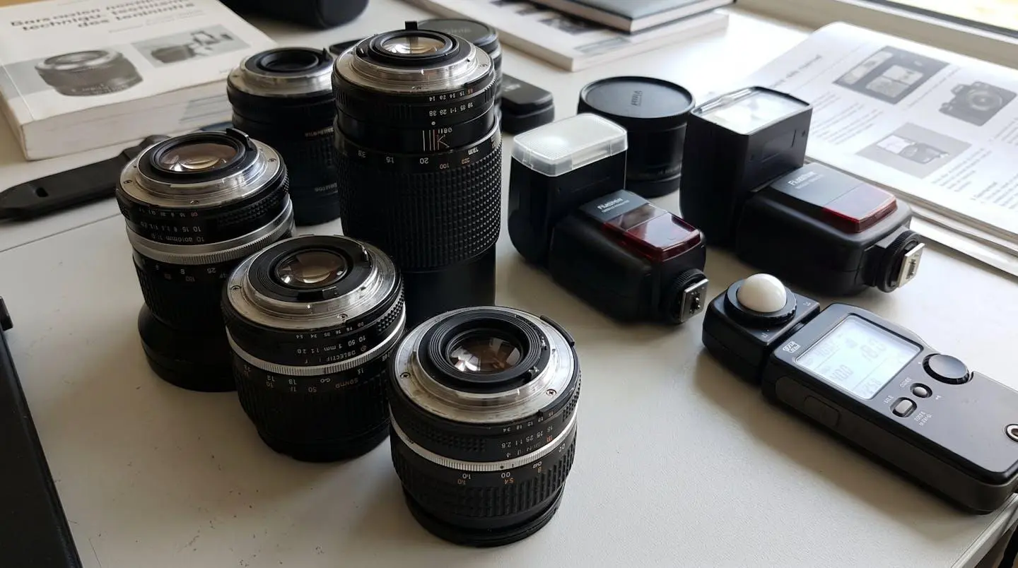 Gros plan sur du matériel photographique professionnel comprenant plusieurs objectifs de focales différentes, flashs compacts et posemètre disposés sur une surface moderne